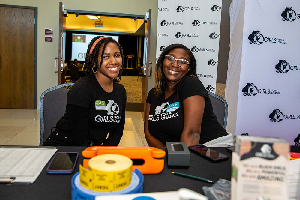 Two smiling Black women greeting attendees to the Black girl rally